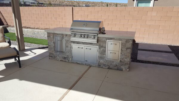 Stone veneer BBQ island with built-in grill and stainless storage doors on a concrete patio in Pahrump