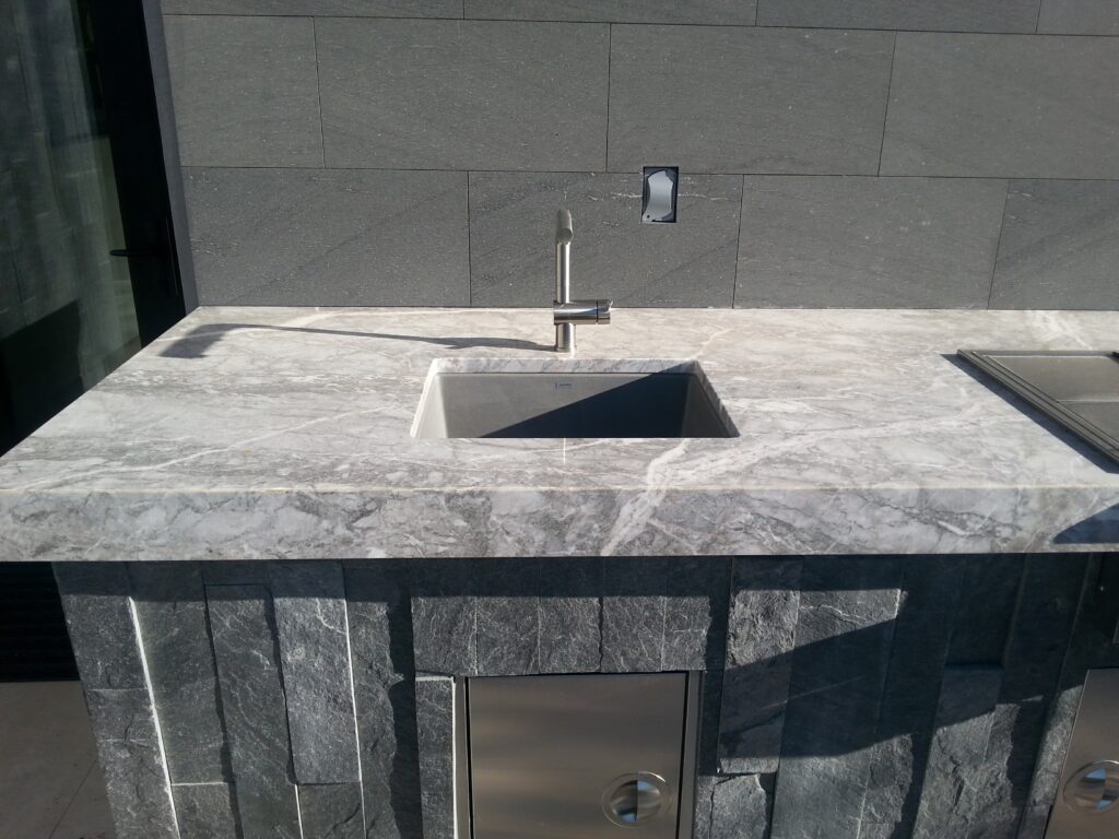 Custom BBQ island with stone waterfall-edge counter and prep sink in Las Vegas