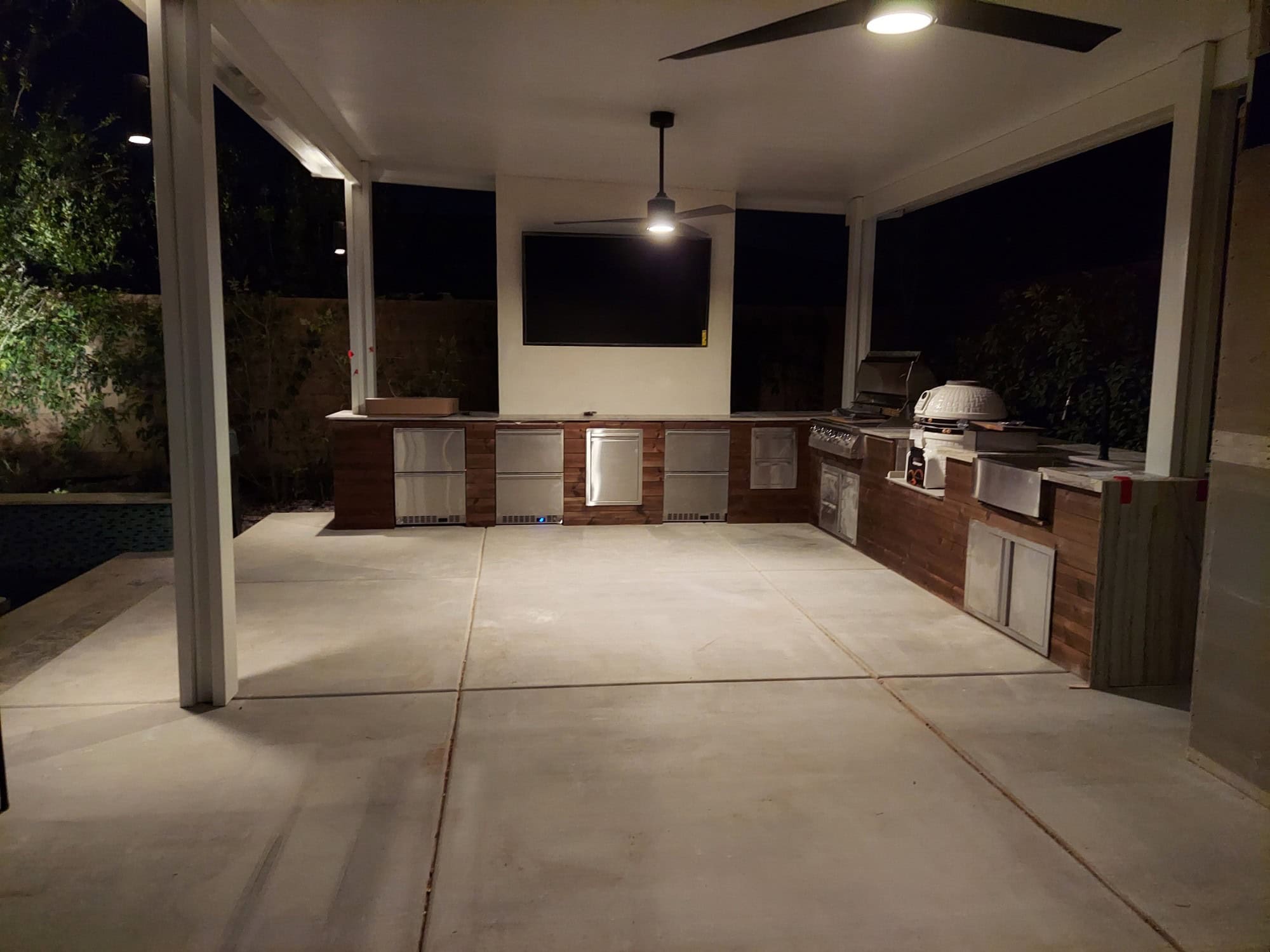 Outdoor kitchen with a Thermory wood media wall and mounted TV lit up at night in Las Vegas