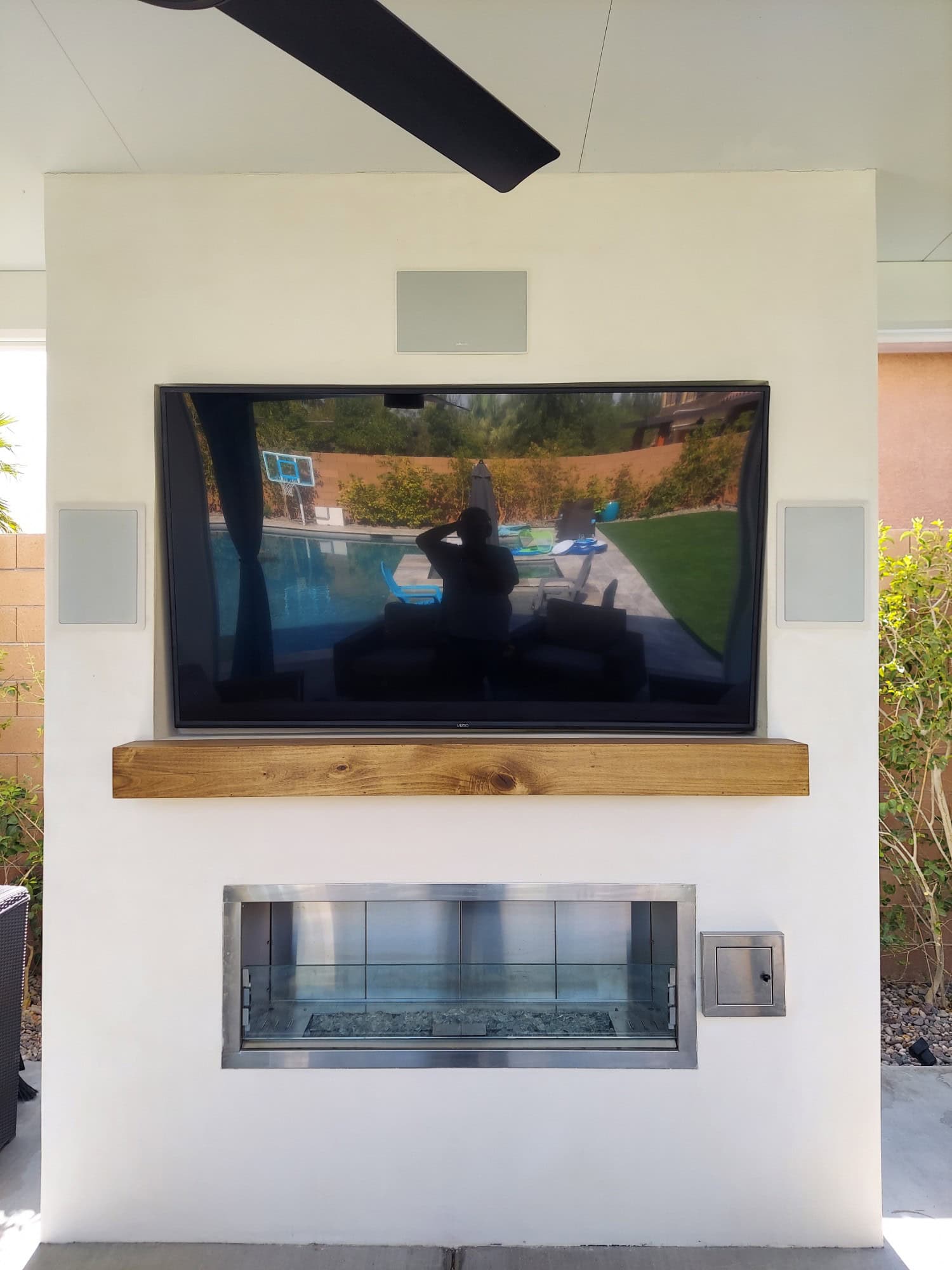 White stucco outdoor media wall with a recessed TV, wood mantel heat block, linear fireplace, and outdoor speakers in Las Vegas