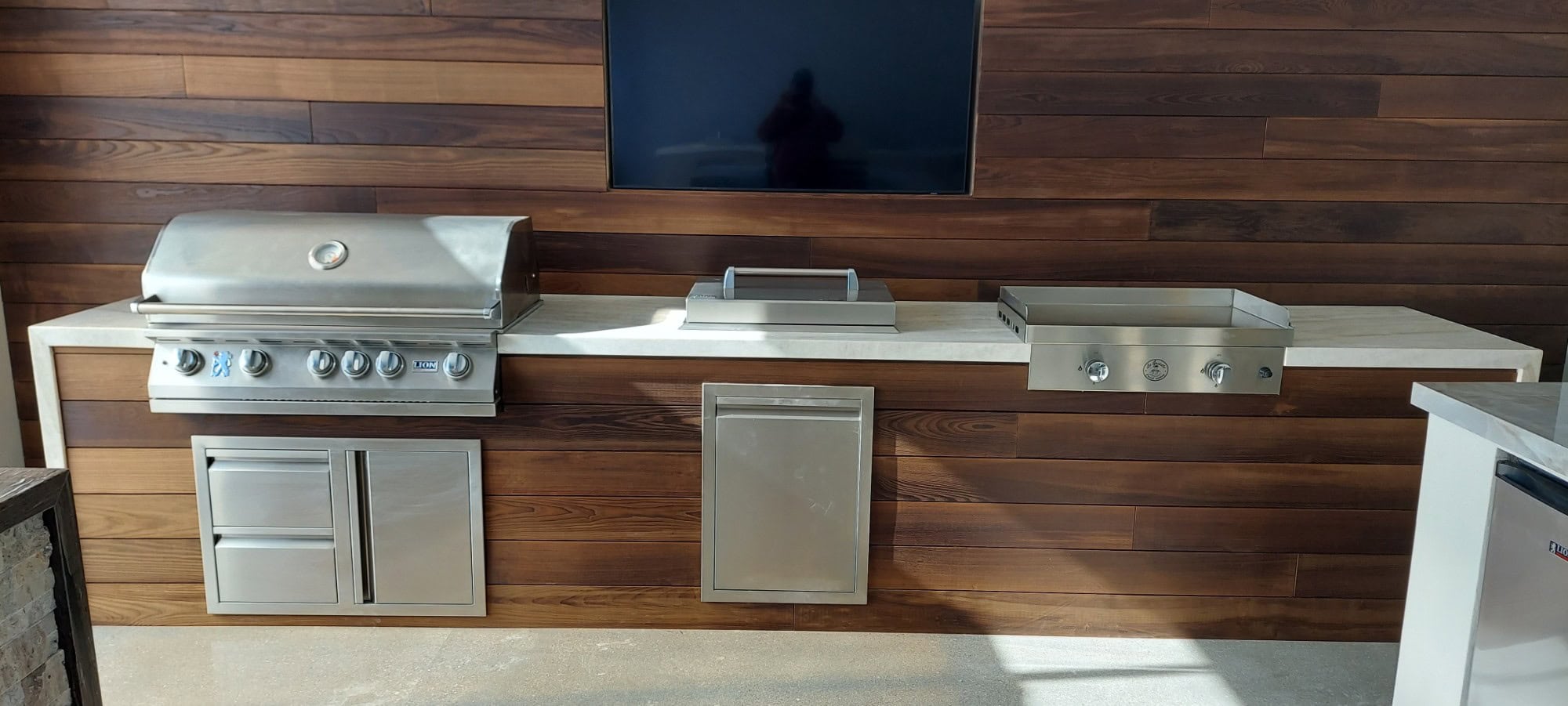 Thermory real-wood outdoor media wall with a mounted TV beside a Lion grill BBQ island in Las Vegas