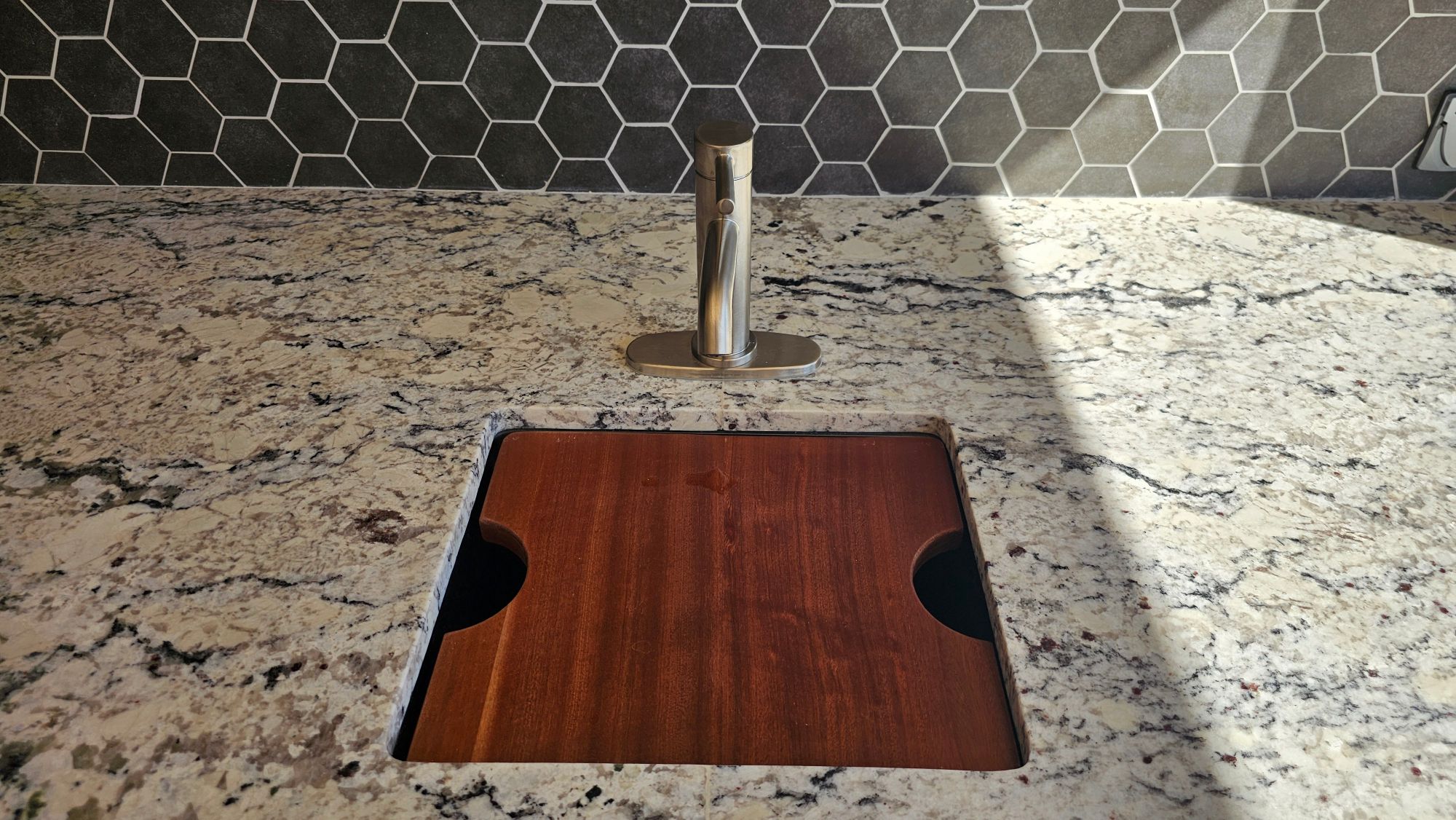 Undermount bar sink with a wood cover and low-profile faucet on a granite outdoor kitchen counter