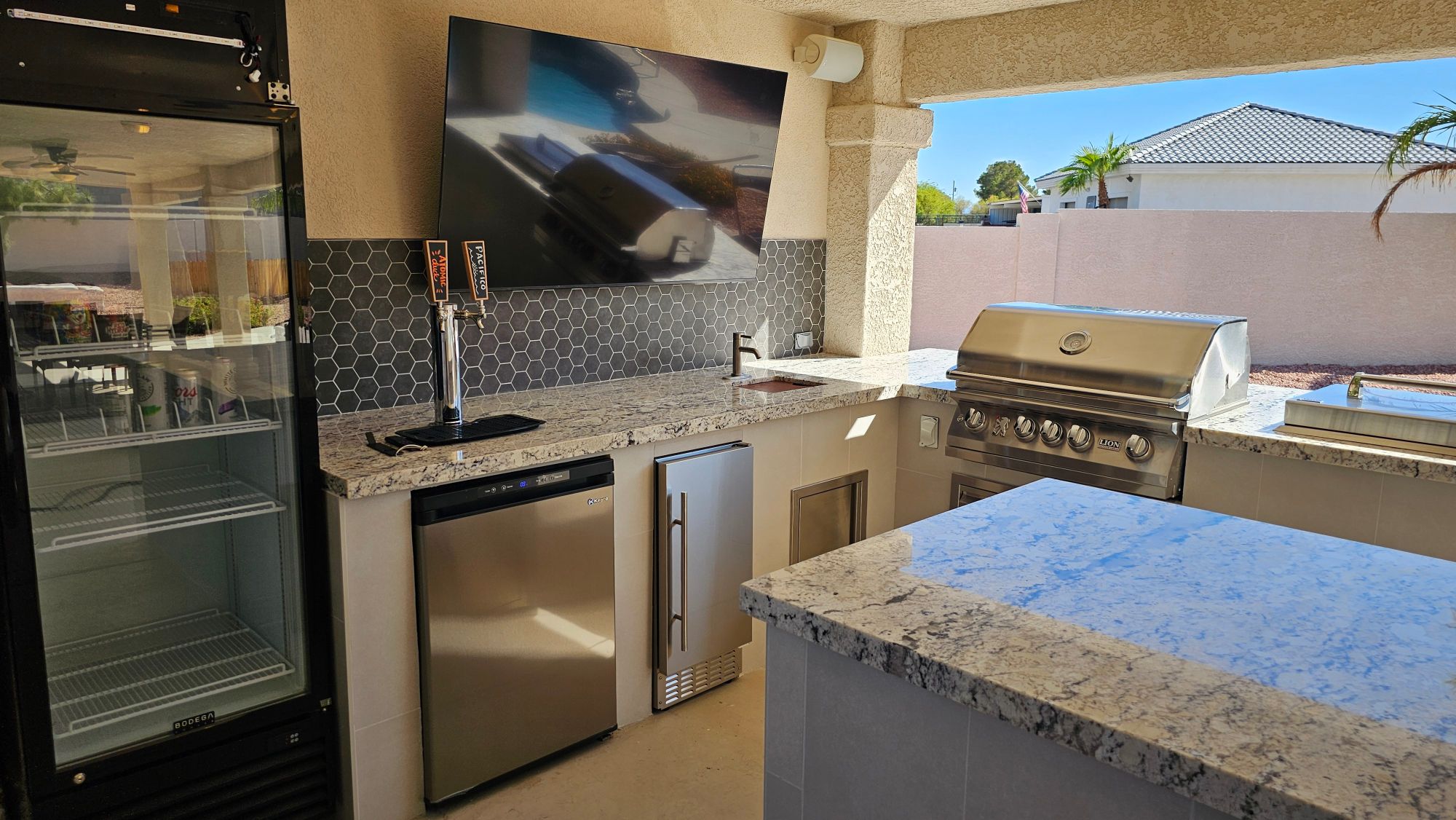 Covered patio outdoor kitchen with mounted TV media wall and Lion grill in Las Vegas