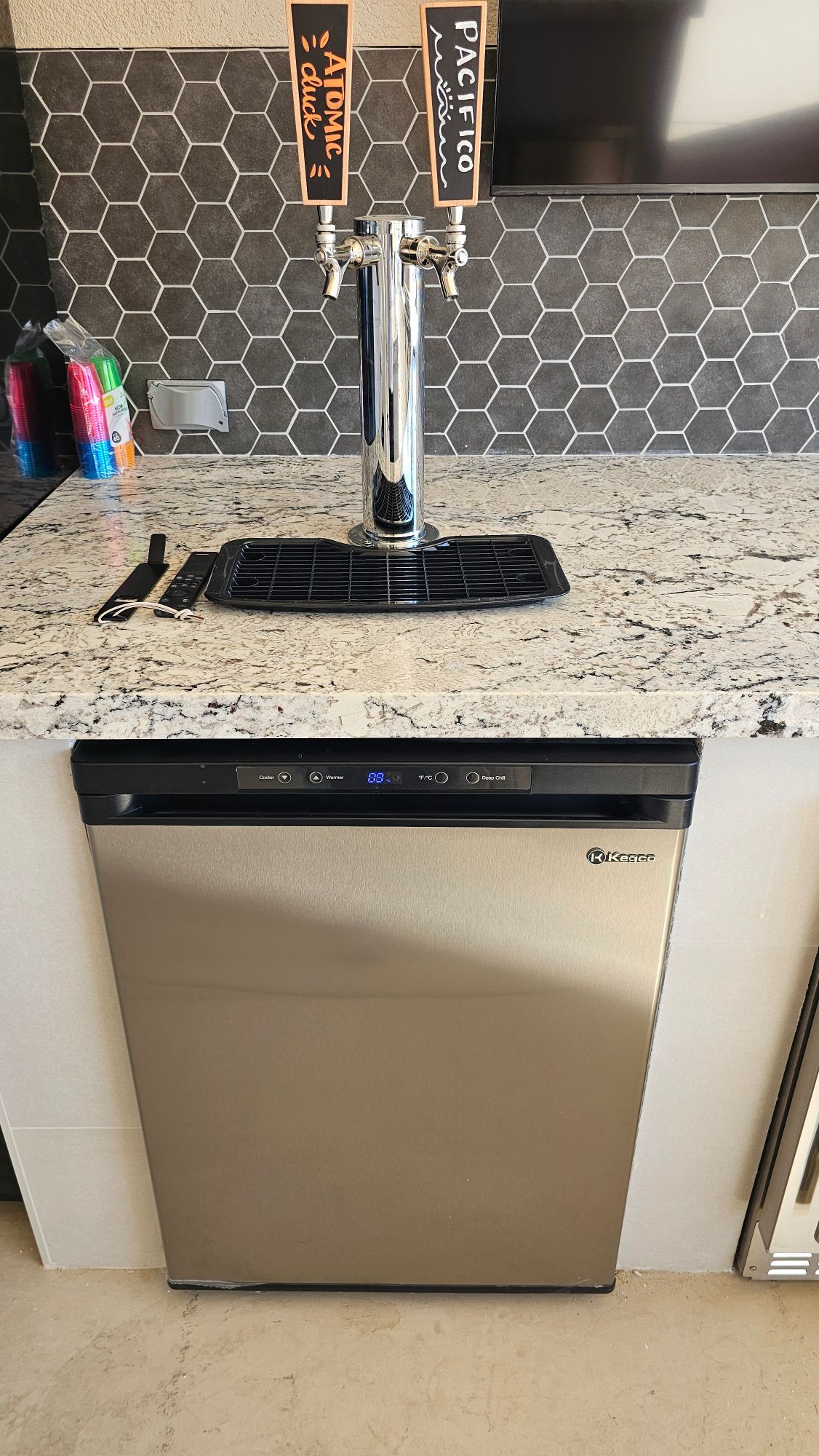 Dual-tap beer system on a granite counter with hexagon tile backsplash in an outdoor kitchen
